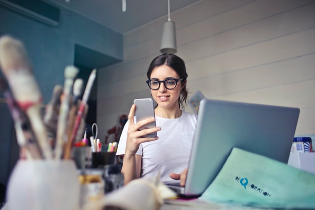 A social media manager works on both her phone and her laptop. 