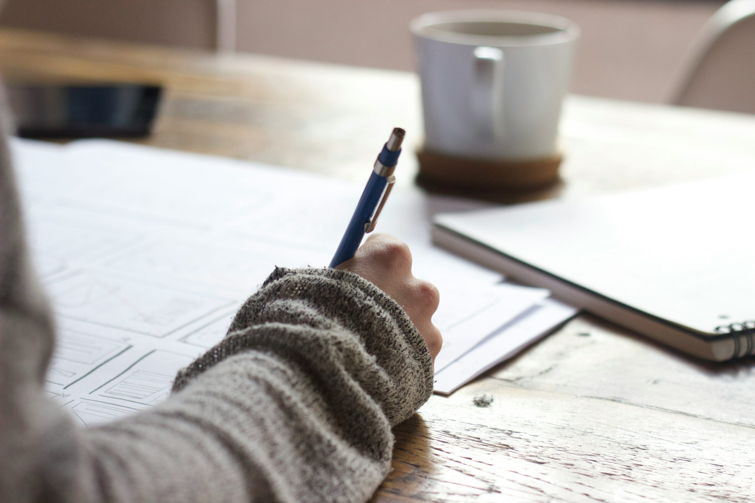 People writing on a brown table with a white mug