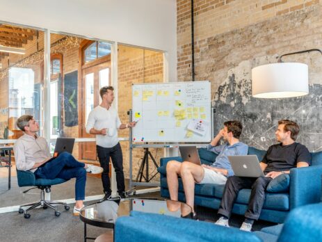 three men sitting while using laptops and watching the man beside the whiteboard