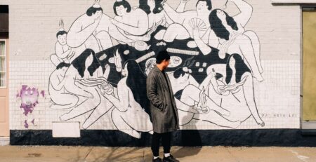 person in a grey coat standing in front of a wall with a mural