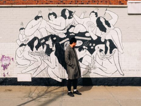 person in a grey coat standing in front of a wall with a mural