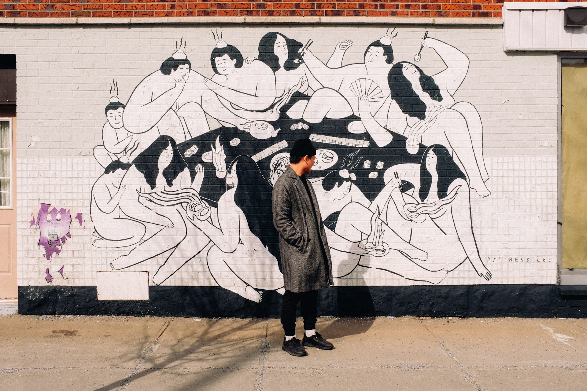 person in a grey coat standing in front of a wall with a mural